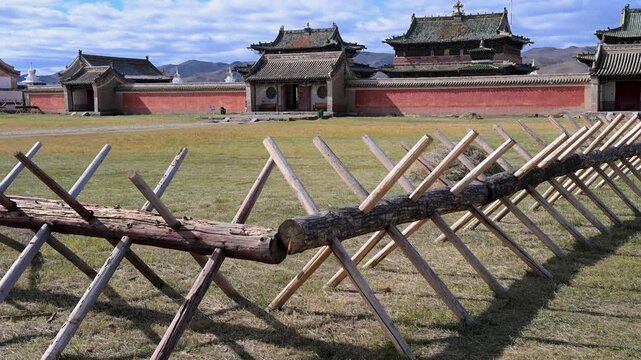 Wide shot of the historic Erdene Zuu Monastery buildings behind a traditional wooden barrier in Kharkhorin, Mongolia. The ancient Buddhist site in the Orkhon Valley