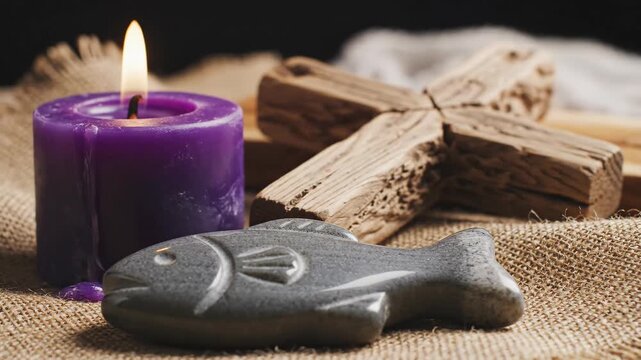 Lit purple candle glows, casting warm light on gray fish-shaped object and natural wooden pieces. This arrangement evokes spiritual and calm atmosphere, suitable for religious video or sacred themes.