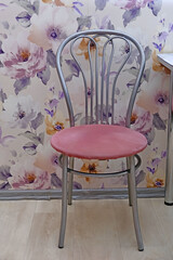 Pink upholstered metal chair against a floral wallpaper. Interior design and home decor concept for living space or kitchen.