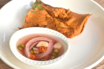 grilled curry fish and egg horseshoe crab wrapped in banana leaf on plate dipping spicy chili sauce