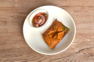 grilled curry fish and egg horseshoe crab wrapped in banana leaf on plate dipping spicy chili sauce