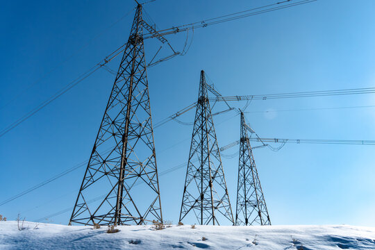 Low angle view of high voltage transmission towers under clear blue sky in winter.