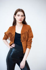Professional fashion model wearing brown jacket and black outfit posing in studio on clean background, elegant young woman portrait for modeling agency portfolio, modern commercial beauty photography