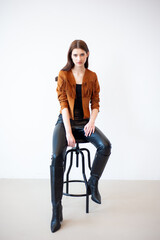 Professional fashion model wearing brown jacket and black outfit posing in studio on clean background, elegant young woman portrait for modeling agency portfolio, modern commercial beauty photography