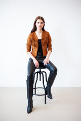 Professional fashion model wearing brown jacket and black outfit posing in studio on clean background, elegant young woman portrait for modeling agency portfolio, modern commercial beauty photography