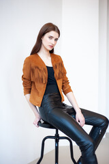 Professional fashion model wearing brown jacket and black outfit posing in studio on clean background, elegant young woman portrait for modeling agency portfolio, modern commercial beauty photography