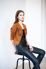 Professional fashion model wearing brown jacket and black outfit posing in studio on clean background, elegant young woman portrait for modeling agency portfolio, modern commercial beauty photography