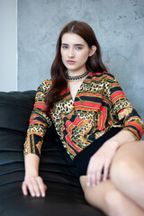 Cozy fashion portrait of a young woman wearing a colorful knitted sweater with ethnic pattern, sitting on a sofa in a studio interior.