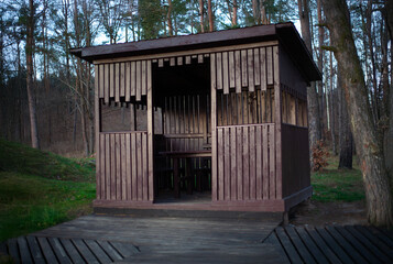 Dark wooden gazebo shelter with table and benches in a pine forest park