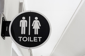 A modern, circular wall-mounted toilet sign featuring white male and female pictograms and the text "TOILET" on a sleek black background. 