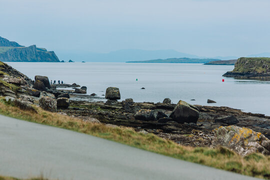 A stunning coastal landscape photograph featuring the rugged beauty of An Corran Beach and Staffin Bay on the Trotternish Peninsula. The image captures the dark volcanic sands and rocky shoreline