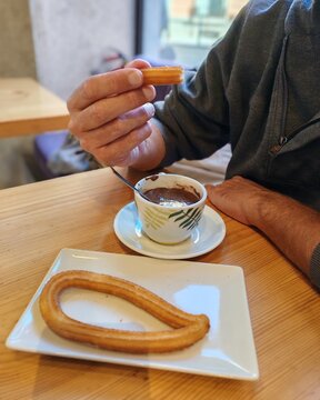 Man eating churros with hot chocolate. A greedy man with churros and hot chocolate in a Spanish pastry shop. A typical Spanish snack or calata, made by a young man. Delicious. Typical.Sweet Andalusia.