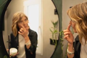 Woman applying facial cream to her nose reflection during daily beauty routine