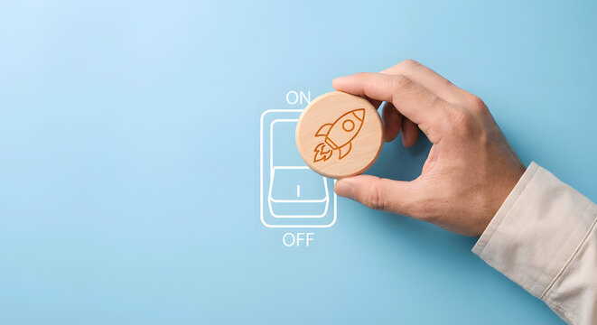 hand holding wooden coin with rocket on switch button