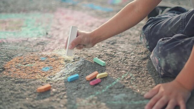 White chalk glides in a child hand, drawing patterns and shapes on the street. Outdoor play brings art color, the kid smiles while chalk designs grow. Chalk covers the street in bright child creations