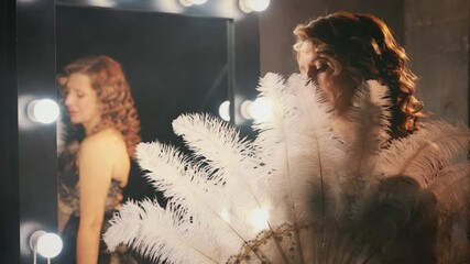 Beauty blonde hair sexy retro lady looking into camera hand holding fan of natural white ostrich feathers. woman burlesque show actress in dressing room. Flapper girl 20s roaring twenties old style