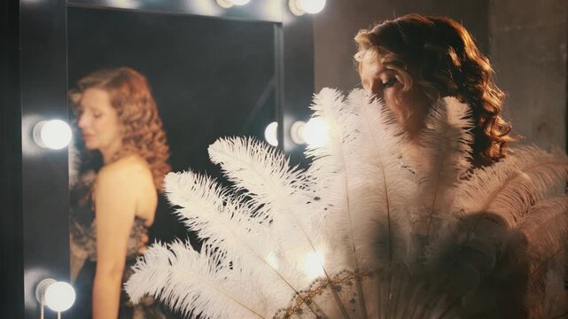 Beauty blonde hair sexy retro lady looking into camera hand holding fan of natural white ostrich feathers. woman burlesque show actress in dressing room. Flapper girl 20s roaring twenties old style