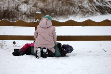 Two children playing in snow near the wooden fence, leisure in winter park