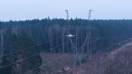 A drone flying past a high-voltage electricity pylon, capturing an aerial view of power transmission infrastructure.