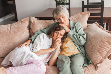 Worried aged mother embracing comforting sad grown up daughter with broken heart family sit on sofa
