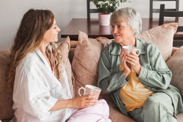 Happy adult daughter and senior mother having fun enjoying talk sit on sofa at home