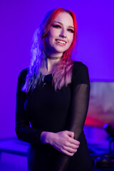 Young woman with vibrant hair in a purple-lit room, posing confidently