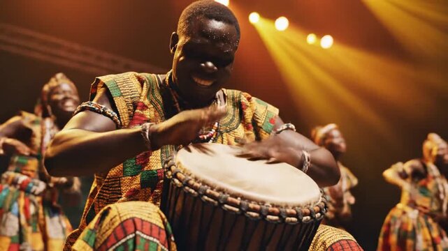 A man enthusiastically plays a drum during a musical performance, surrounded by performers
