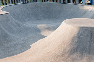 Empty concrete skate park featuring various ramps, bowls, and curves, illuminated by late afternoon sunlight creating deep shadows © EdNurg