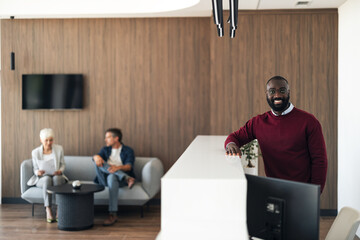 Friendly Black Man At Reception Desk Welcoming Guests In Modern Office Lobby Setting