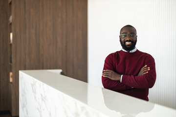 Smiling Man in Burgundy Sweater Leaning on White Marble Reception Desk in Modern Office