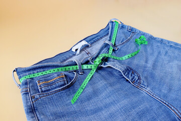 Blue jeans with measuring tape on color background.