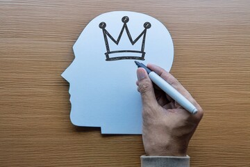 Conceptual image of a hand drawing a crown inside a head. Narcissism, ego, self-importance, mental health, and superiority complex concept.