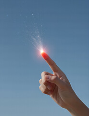 Hand pointing at glowing particles against blue sky