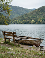 Old wooden rowboat on lakeshore with wooden bench, forested hills in background