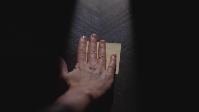 Slow motion close up footage of a hand writing out "Hello" on a paper note and placing it on a table. Shot in dramatic lighting for an impressive title or transition.