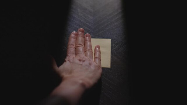 Slow motion close up footage of a hand drawing a heart on a paper note and placing it on a table. Shot in dramatic lighting for an impressive title or transition.