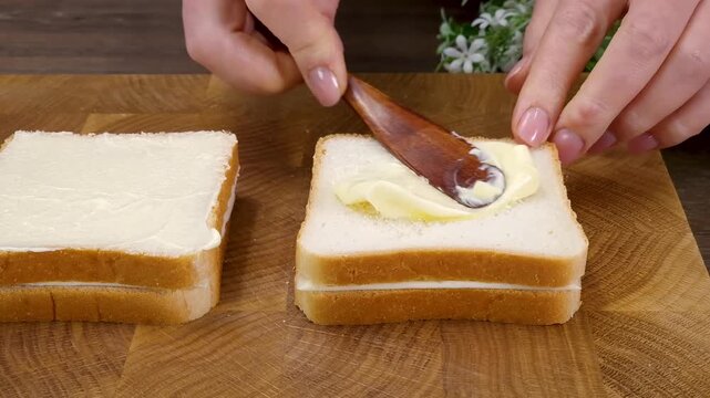 Woman spreading fresh butter on white bread slice with wooden spoon in kitchen