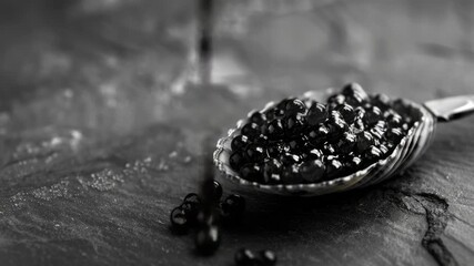 A spoonful of caviar is ready to be served on a dark-colored table. The contrast between the shiny caviar and the matte table adds depth to the .