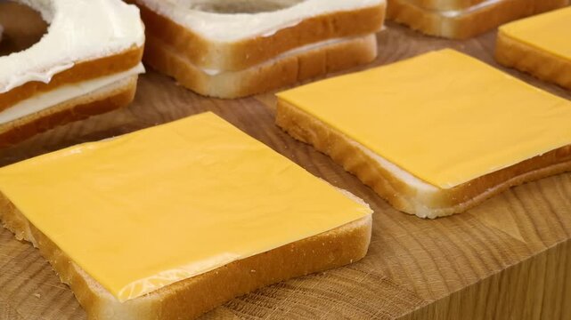 Woman placing cheddar cheese slice on bread and stacking hollow toast in kitchen