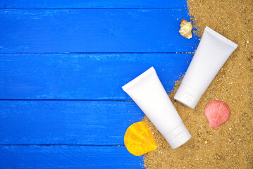 Cream tube and sand on blue wooden. Sea summer vacation background with space for the text. Top view