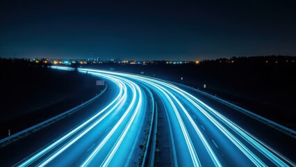 Obraz premium Blue light trails of vehicles on a curved highway at night with distant city lights in the background