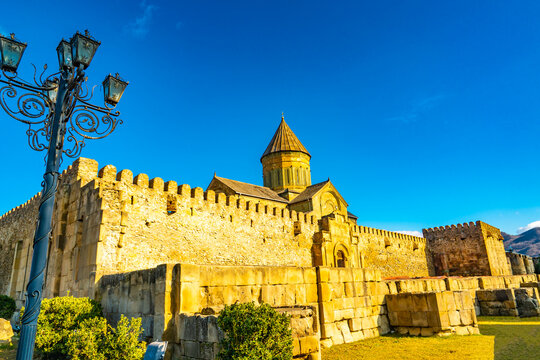 Warm afternoon light illuminates the fortified stone walls and conical dome of Svetitskhoveli Cathedral, a major Georgian Orthodox church and part of the UNESCO‑listed Historical Monuments of Mtskheta