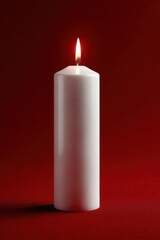 A white candle is lit on a red background