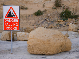 warning sign for falling rocks at coastal cliff with large boulder © Comofoto