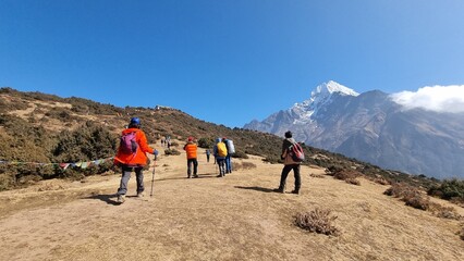 Group of hikers trekking through a scenic mountain trail under a clear blue sky, with majestic snow-capped peaks in the distance, embodying adventure and exploration