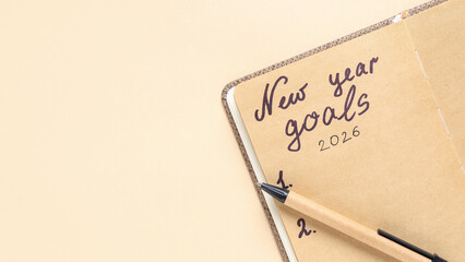 Notebook with Text NEW YEAR GOALS 2026 on Beige Background, Closeup