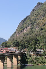 Panoramic autumn mountain landscape featuring a high peak view over a misty forest valley with green trees and a lake under a cloudy sky in Laos