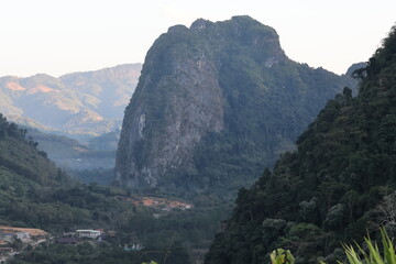 Panoramic autumn mountain landscape featuring a high peak view over a misty forest valley with green trees and a lake under a cloudy sky in Laos