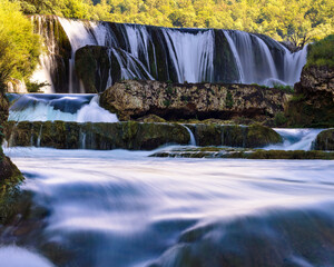 Vertical view of silky river flow below &Scaron;trbački Buk waterfall, long exposure water over mossy rocks in forest canyon on the Una River, Bosnia and Herzegovina, calm nature travel background.
