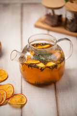 Herbal citrus tea brewed with orange slices and fresh herbs served in a glass teapot on rustic wooden table